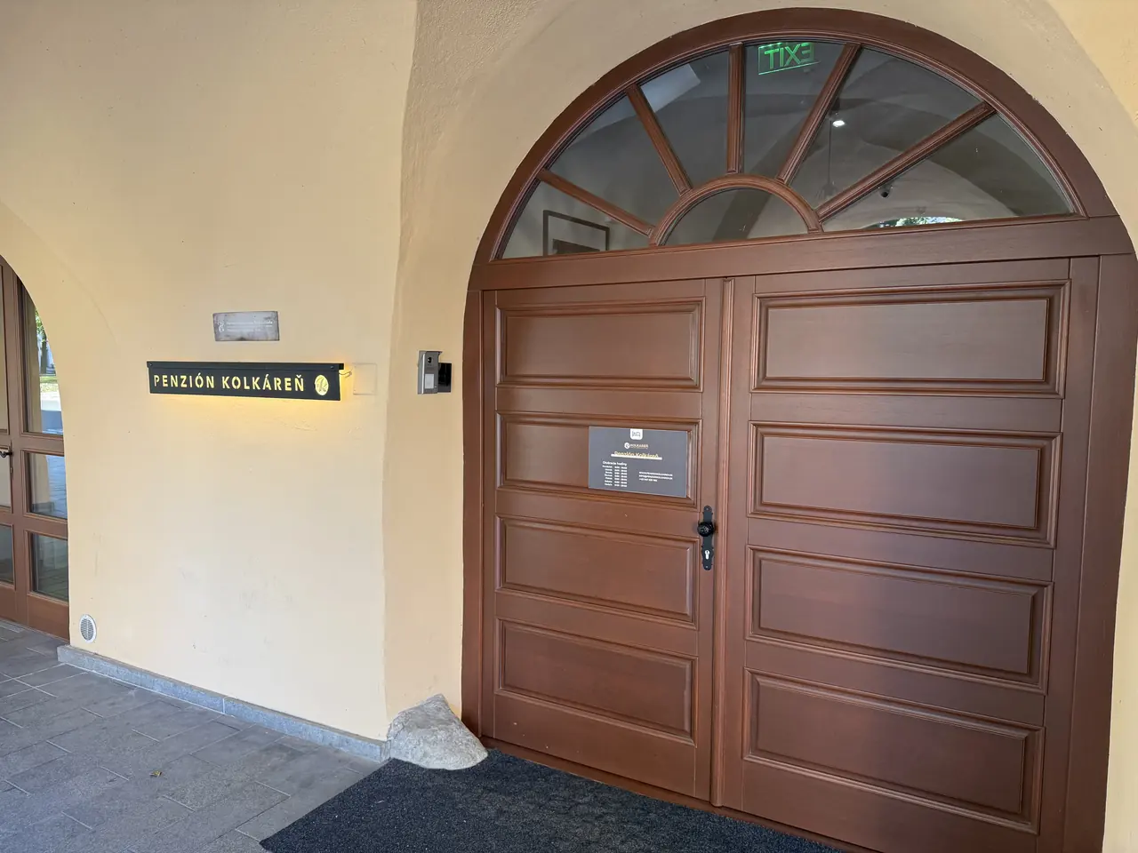 Main entrance under the arch with the illuminated Penzión Kolkáreň sign, the keypad is on the left of the door